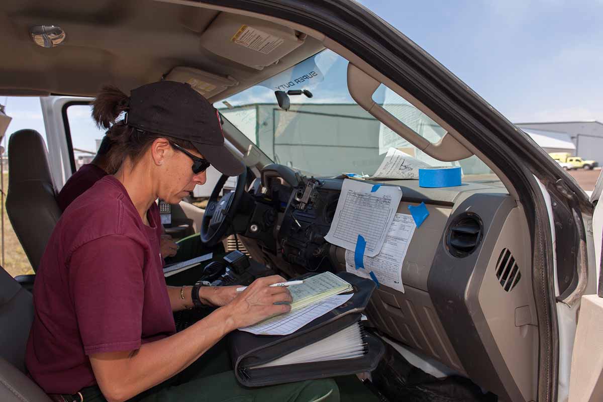 Challenged by a pretty good breeze and lack of decent writing surface Angie Tom of Twin Falls Helitack runs the deck operations from the passenger seat of Durango Helitack's vehicle.